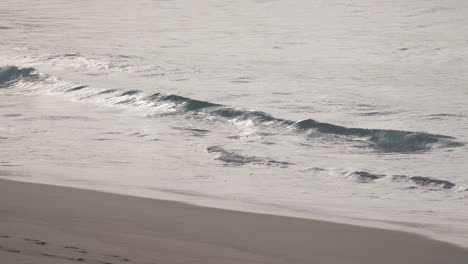 small waves roll out a perfectly smoothly sandy beach with no one insight