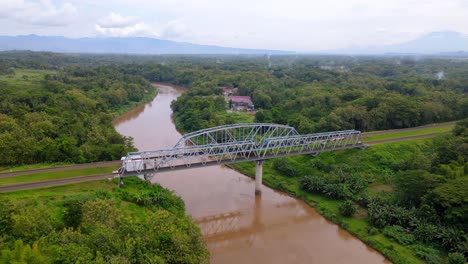 drone view orbiting train track bridge over river with brown water, indonesia