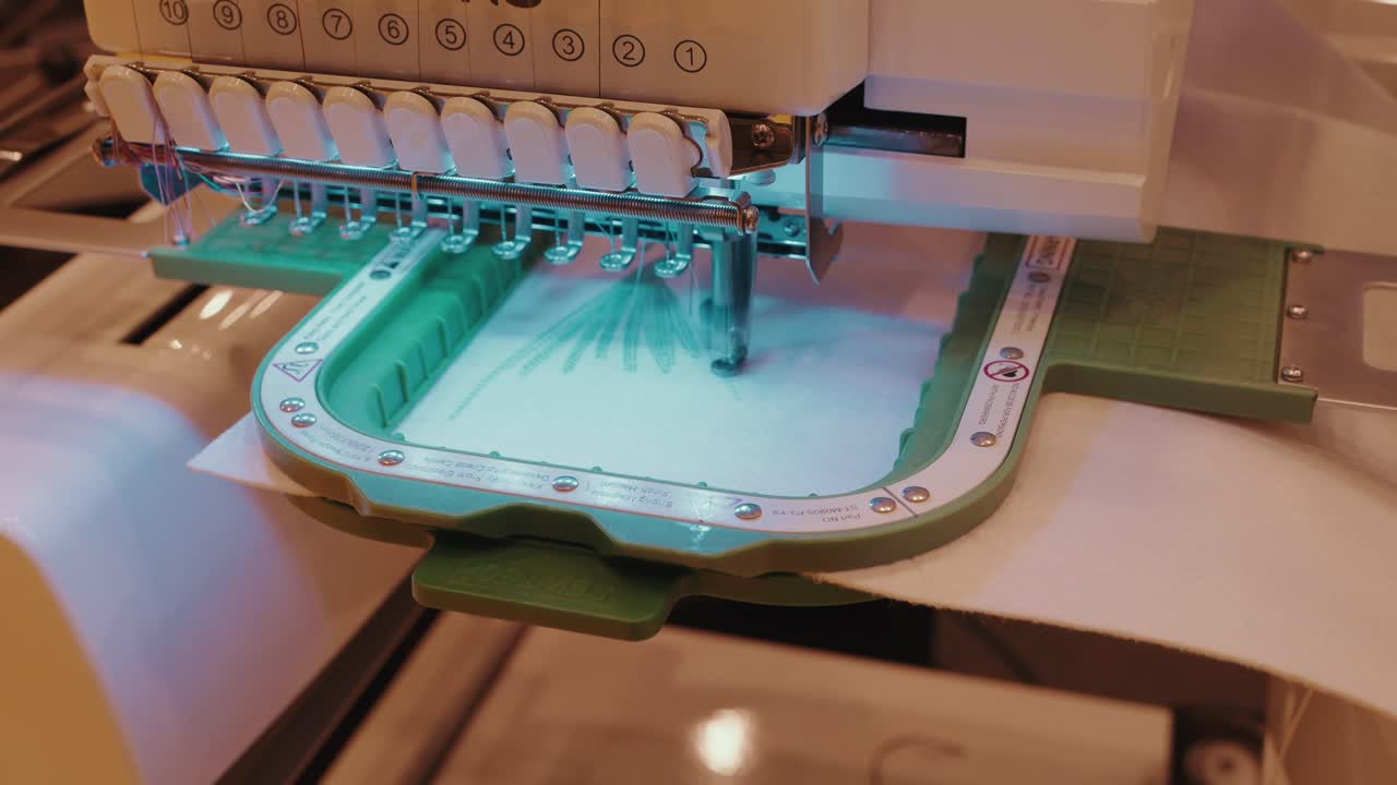 automated embroidery machine sewing teal design on white fabric