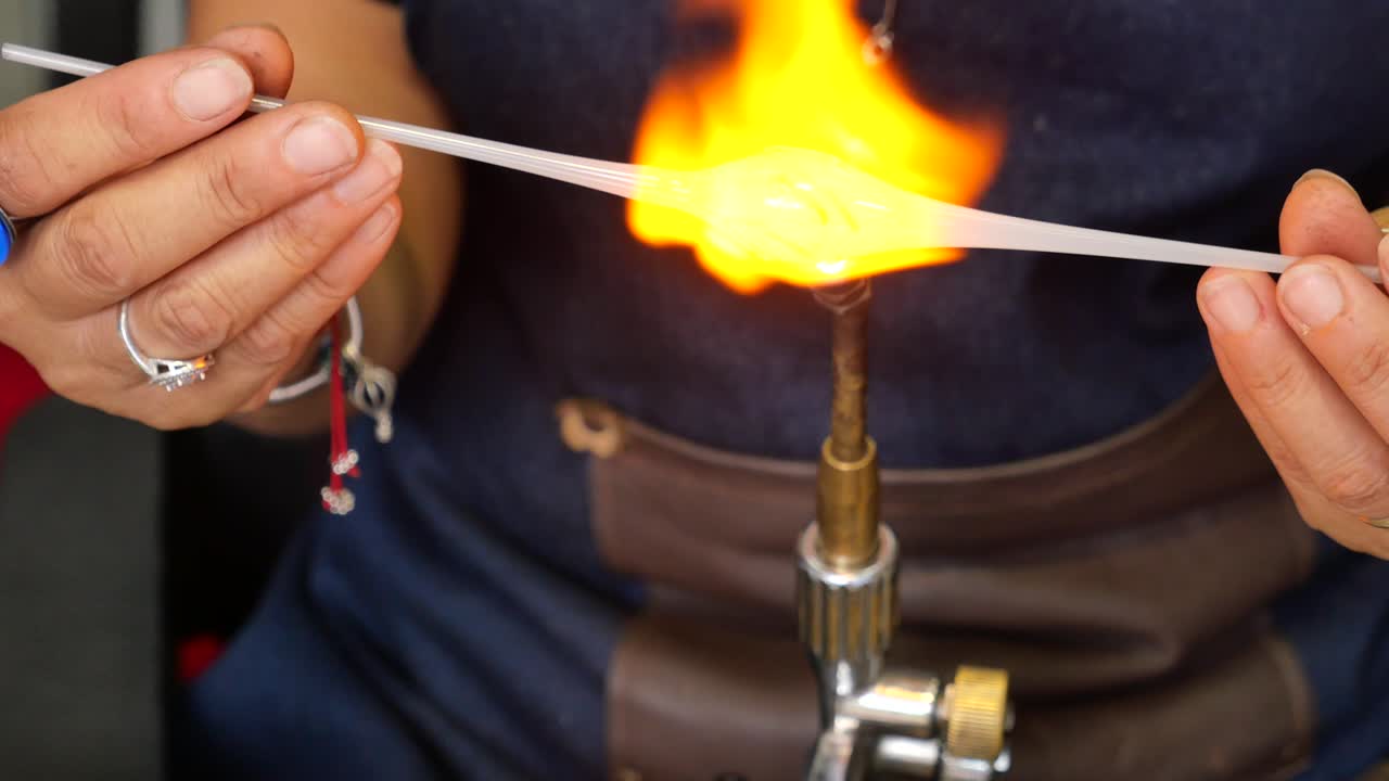 un soplador de vidrio utiliza una antorcha para calentar y derretir vidrio en un taller