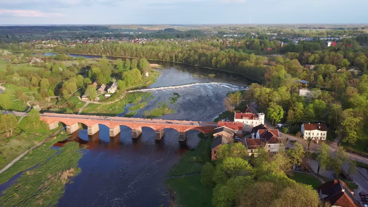clip aéreo 4k, volando sobre la pequeña ciudad de kuldiga letonia, puente de ladrillo rojo sobre el río venta, amplia cascada