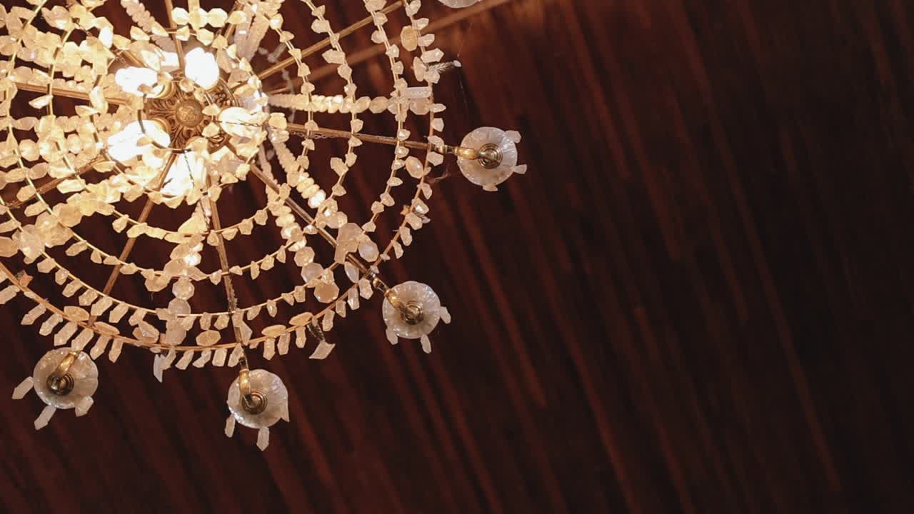 Close up of a glowing crystal chandelier with warm lights against a wooden ceiling background