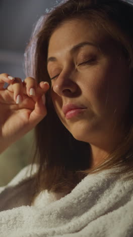 mujer molesta se limpia las lágrimas de las esquinas de los ojos con el dedo sentado en el sillón por la noche en la premisa. noticias tristes que perturban las vacaciones. estado depresivo cámara lenta
