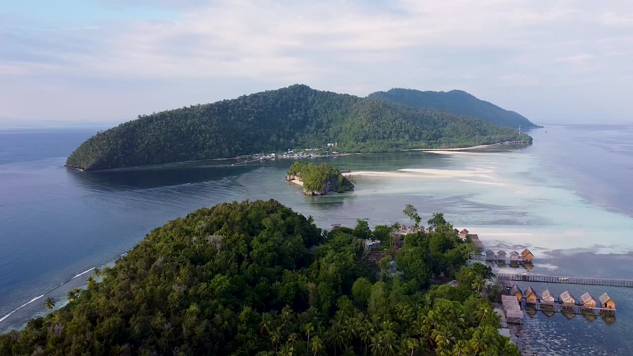 vista aérea reversa sobre islas tropicales cubiertas de selva tropical con cabañas frente al mar con vistas al océano y los arrecifes de coral en raja ampat, papúa occidental, indonesia