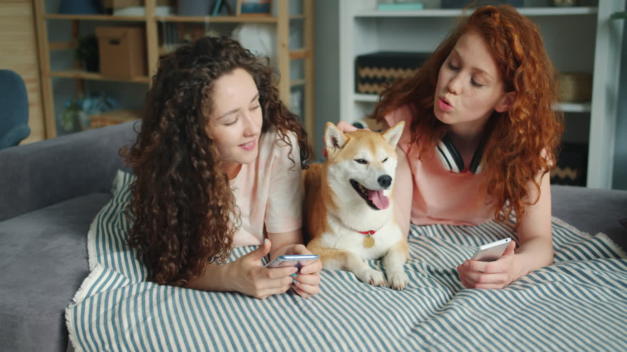 Two girls and a dog using smartphones on a couch