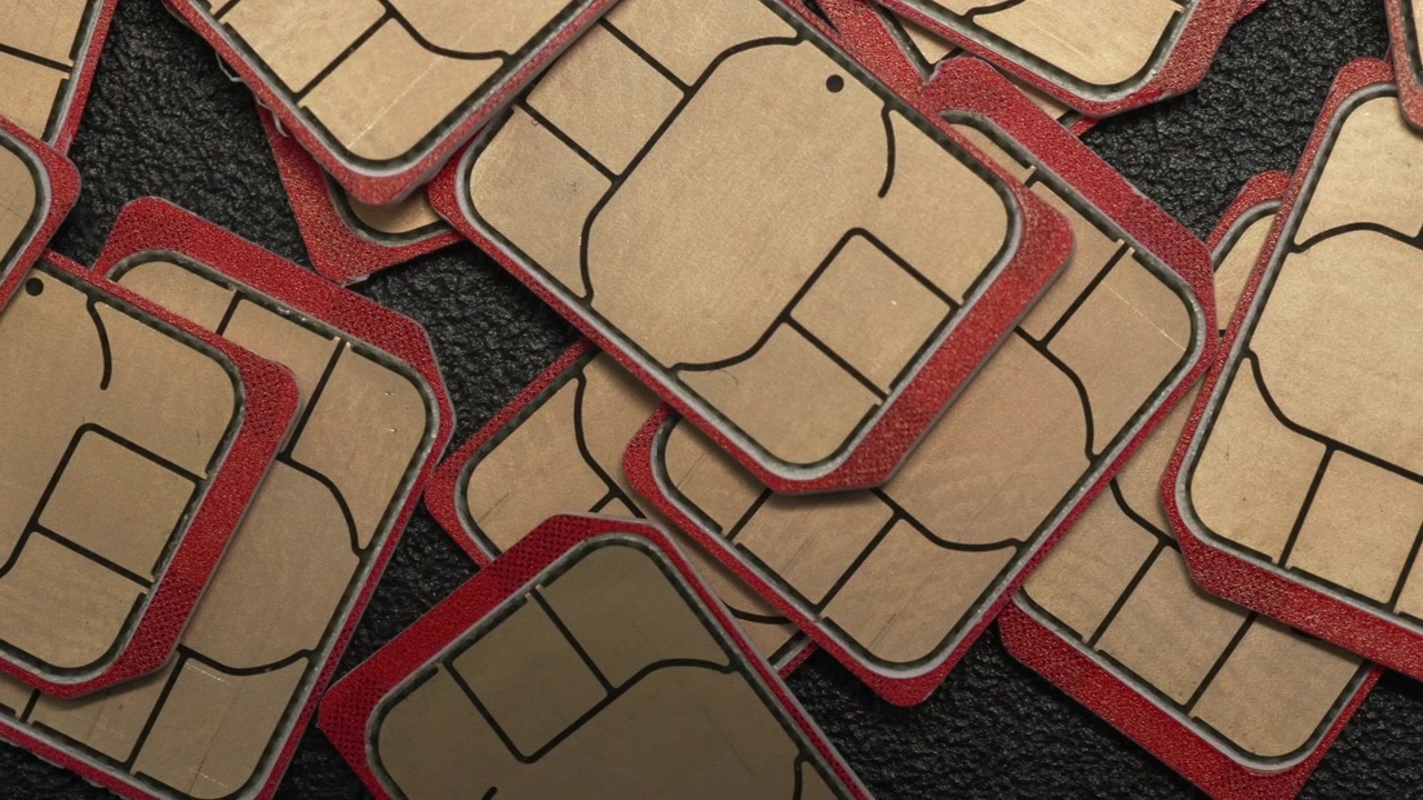 Uma coleção de cartões SIM com bordas vermelhas distintas espalhados sobre uma superfície preta texturizada. Ideal para temas de tecnologia ou telecomunicações