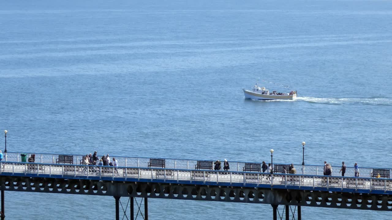 llandudno pier seafront boardwalk를 따라 걷는 관광객을 지나가는 관광 보트 크루즈