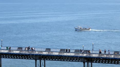 llandudno pier seafront boardwalk를 따라 걷는 관광객을 지나가는 관광 보트 크루즈