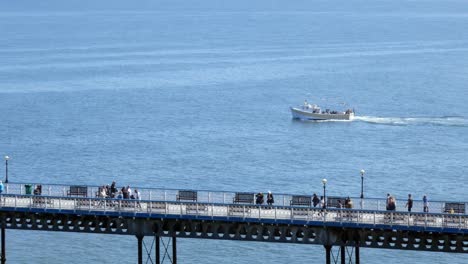 sightseeing boat cruise passing tourists walking along llandudno pier seafront boardwalk