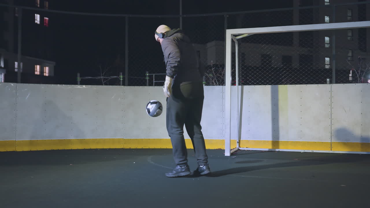 Athlete performing football juggling on an outdoor court at night under bright lights, capturing precision, skill, and focus with urban background, shadowed goalpost, and vibrant yellow court