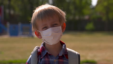 portrait of a little boy wearing a face mask in a school yard