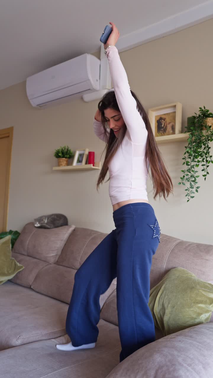 Giovane donna felice che balla sul divano con le cuffie