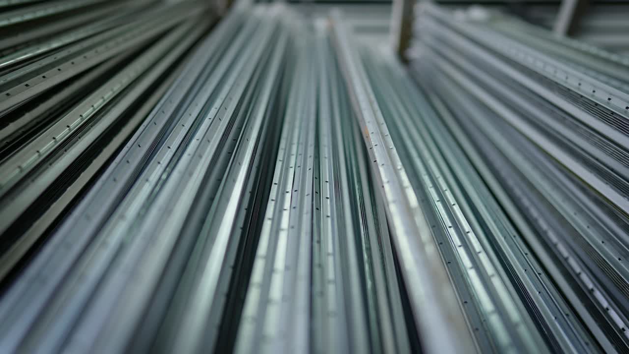 Manufactured stainless steel aluminum corner profiles lying in warehouse indoors. Live camera moves along construction building material stack in industrial storage.