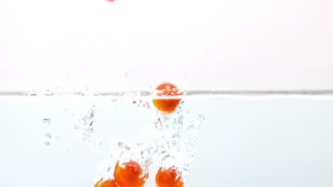 cherry tomatoes falling in water on white background