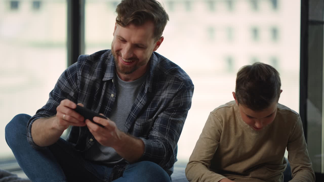 Papà e figlio/a che giocano a un gioco per cellulare al chiuso