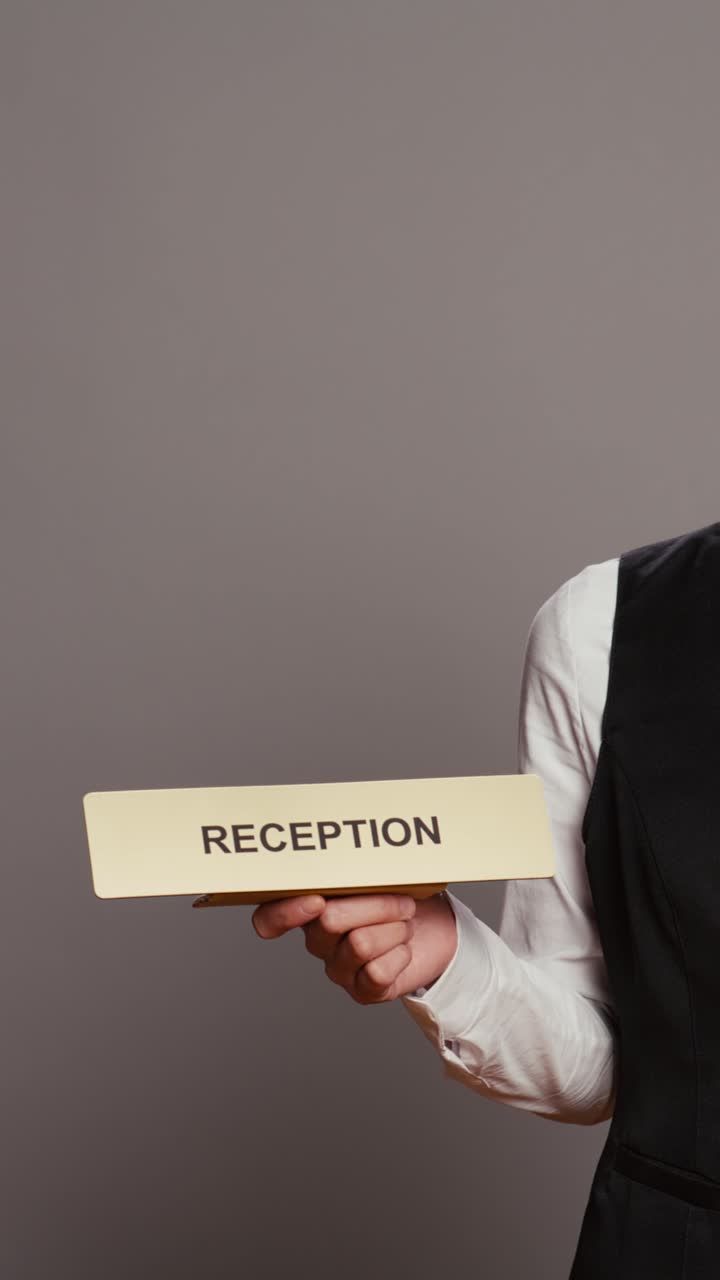 Vertical Video Hotel concierge holding sign to indicate direction for reception desk