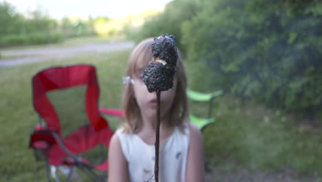 little girl holding up a burnt marshmallow on a stick