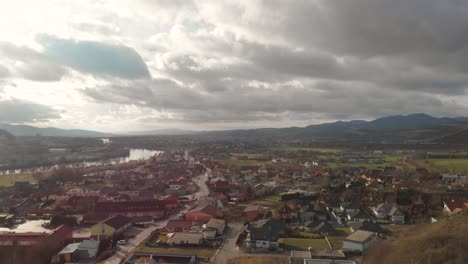 Aufsteigende-Luftdrohne-über-Einem-Wunderschönen-Sonnigen-Kleinen-Dorf-Mit-Großen-Hohen-Wolken-Und-Einem-Fluss