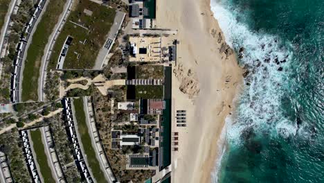 Straight-Down-Aerial-View-of-Beachfront-resort-with-sand-ocean-and-waves-crashing