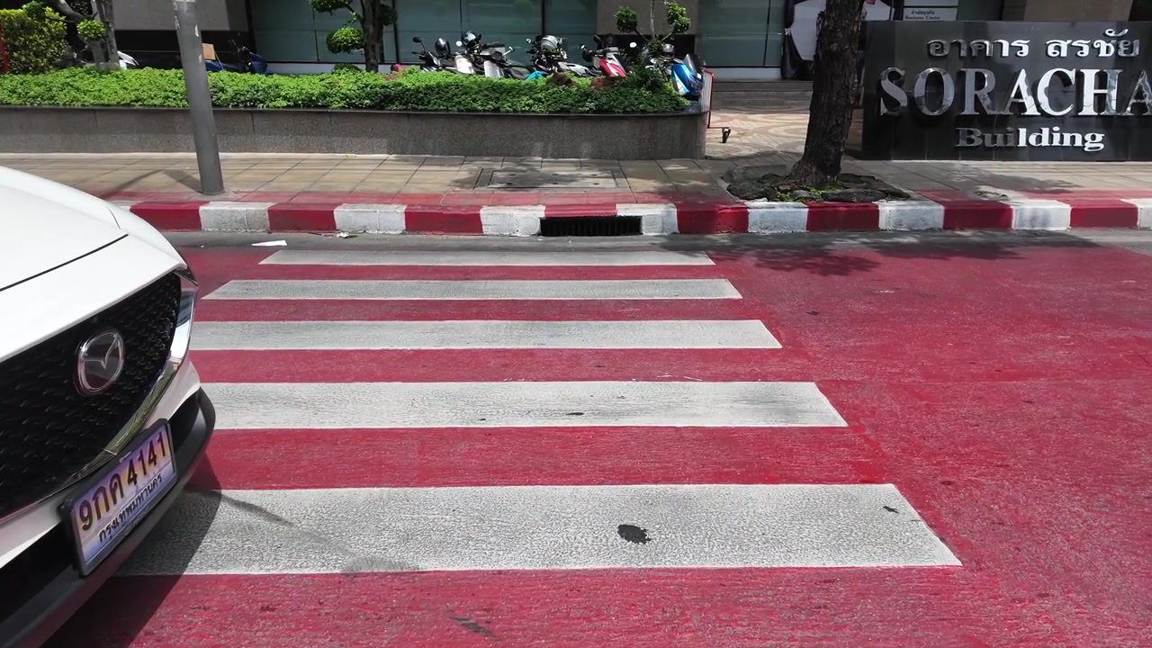 Static shot of a red and white zebra crossing on a city street in Bangkok.