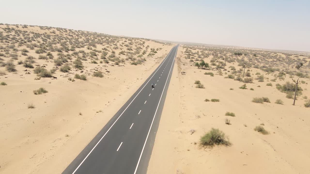 Aerial drone shot displaying a rider on a motorbike crossing through the dry, arid roads of Rajasthan.