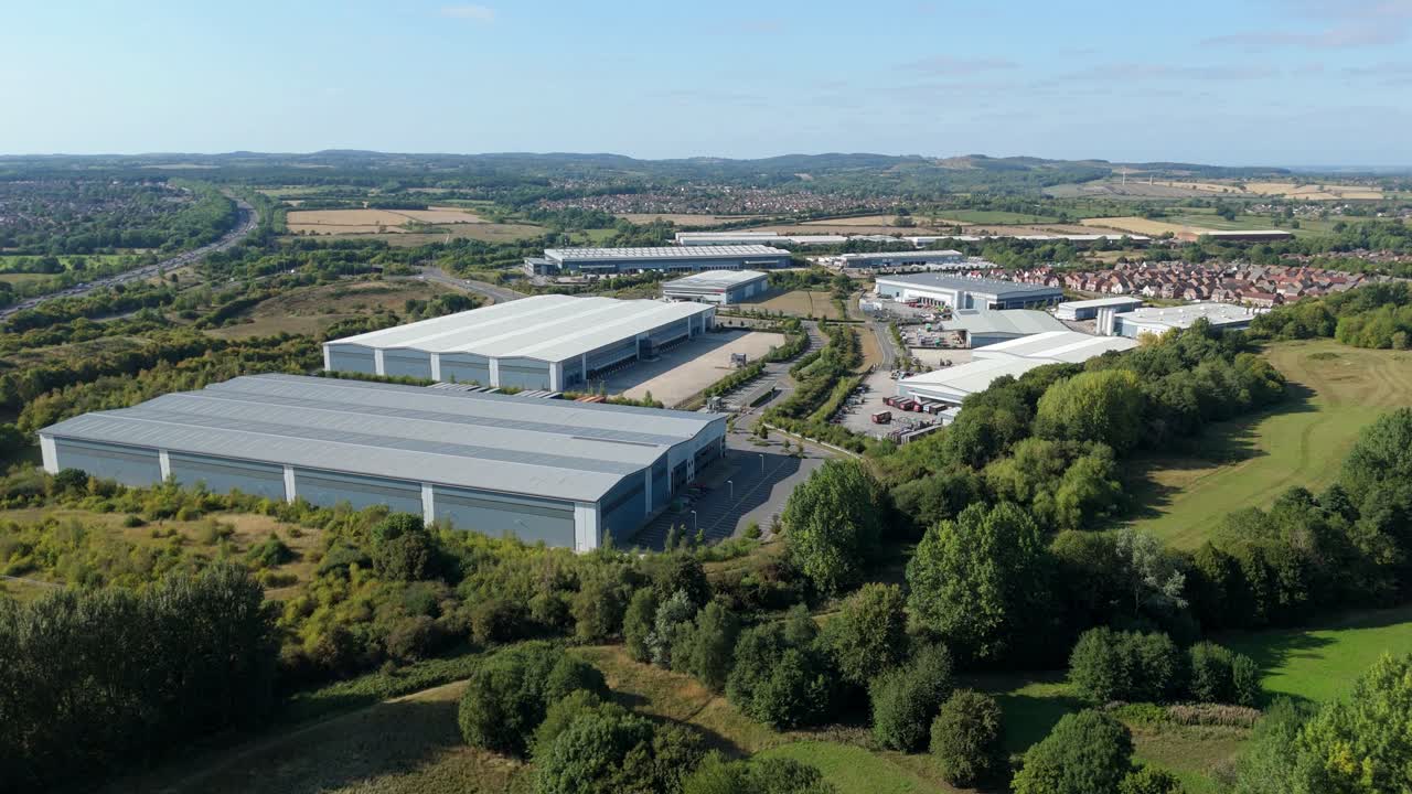 Video aereo di un drone sull'autostrada M1 vicino a Leicester, Inghilterra, Regno Unito, con traffico intenso che scorre accanto a magazzini, centri di distribuzione e zona industriale al tramonto