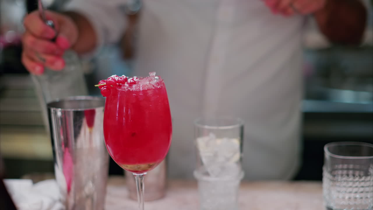 Close up of a red cocktail with a blurry view of a barman preparing a drink in the background