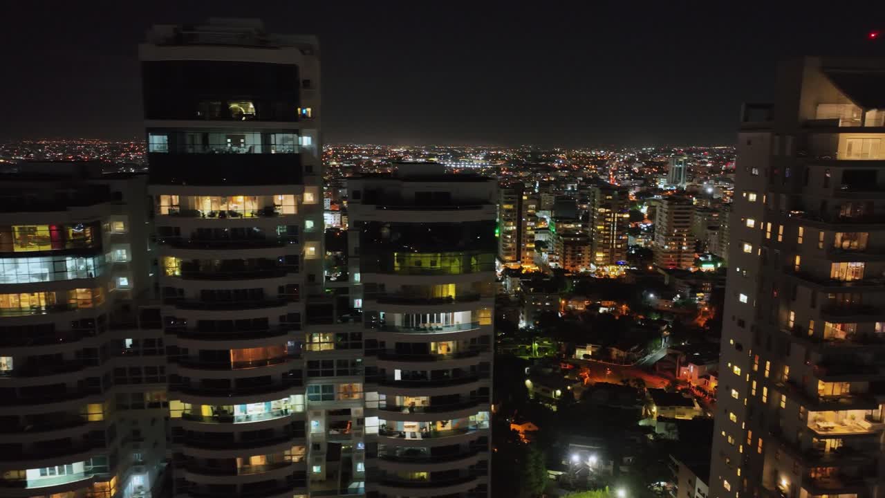 toma aérea de camiones de modernos apartamentos de lujo de gran altura y hermosa ciudad iluminada de santo domingo en segundo plano por la noche