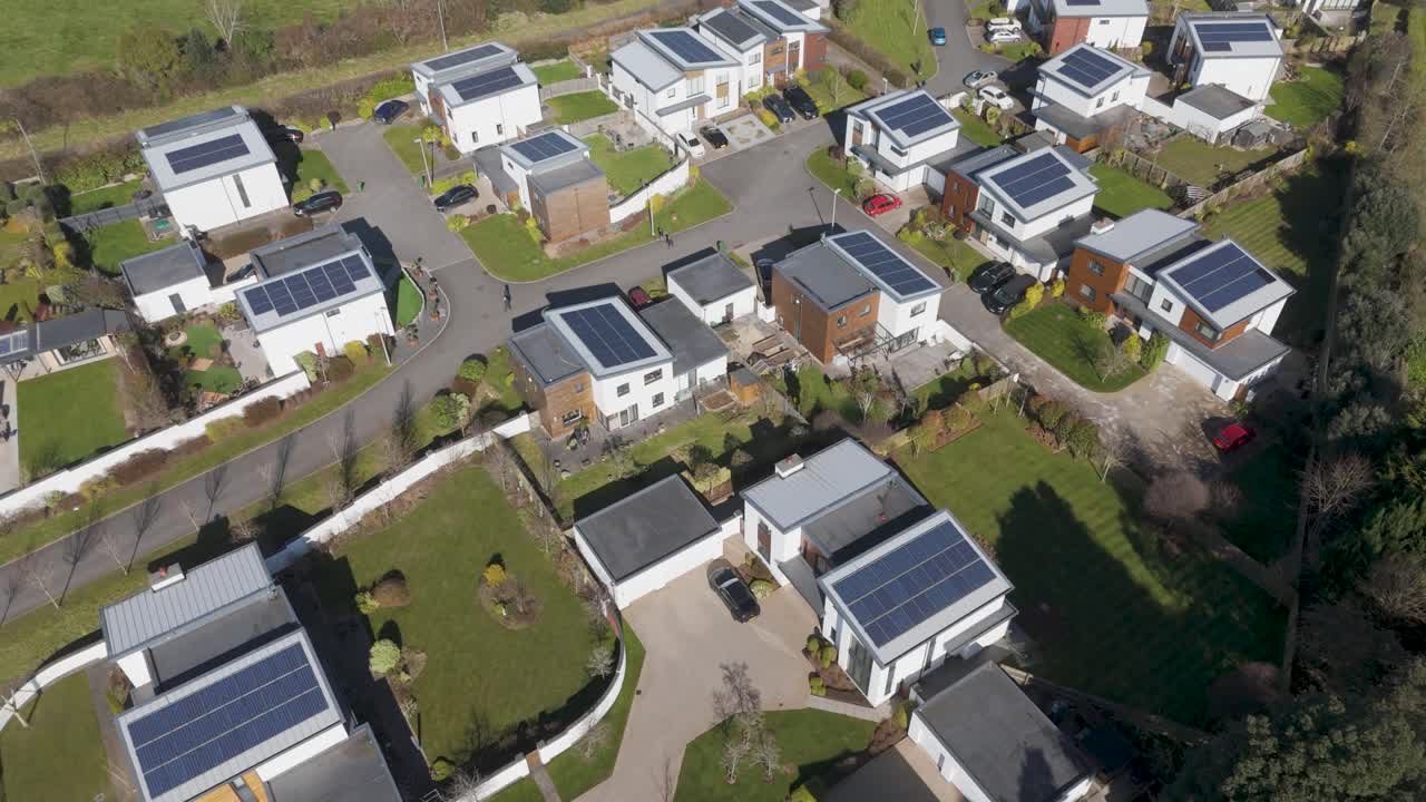 Top-down aerial of pristine luxury estate with white cube-style homes, dark photovoltaic roofs, looping roads and manicured lawns expressing upscale sustainable suburbia