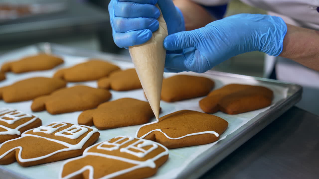 Decorating freshly-baked cookies with white cream. Confectioner squeezes icing from a pastry bag on the gingerbread cake. Close up.