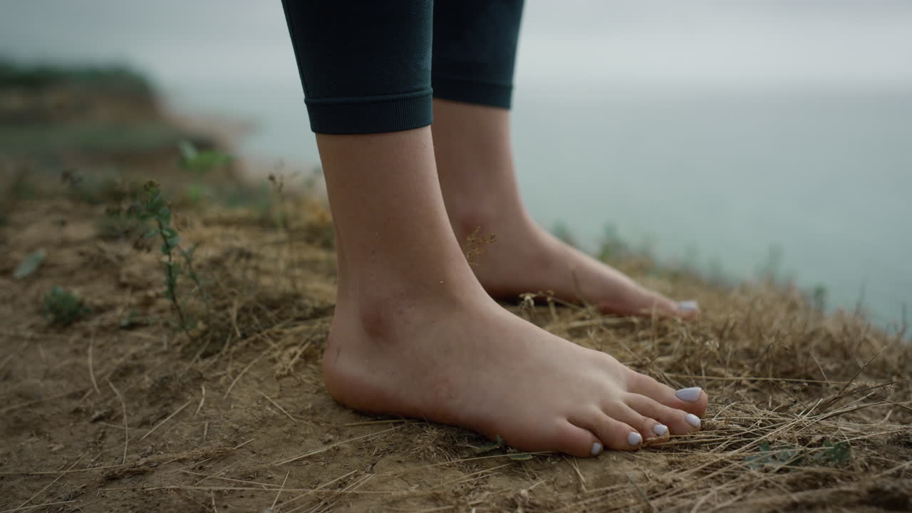Girl legs standing hilltop closeup. Unknown barefoot woman relaxing on sea beach