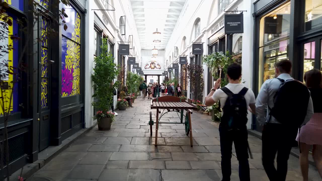 Designer boutique shops in Covent Garden, showing tourists browsing and walking through the undercover market street, London, UK