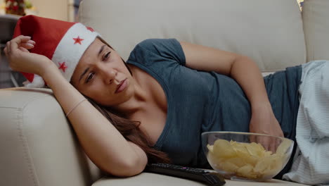 sleepy person wearing santa hat and sitting at tv with chips