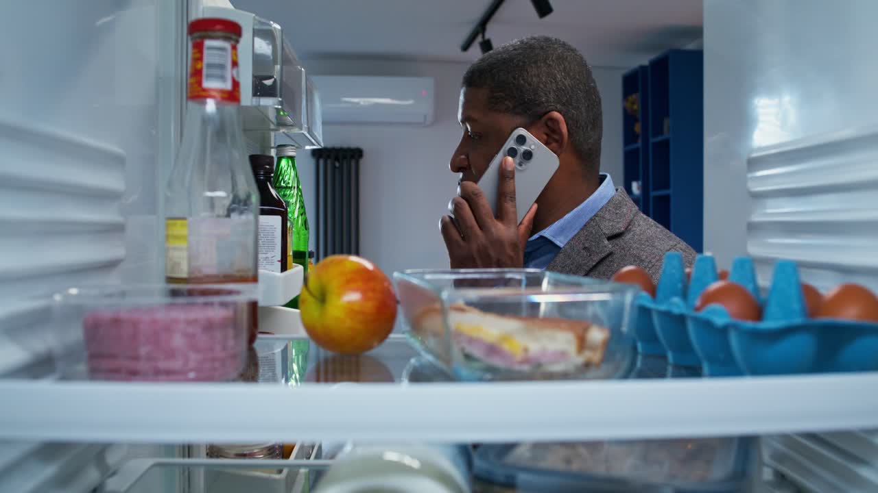 Uomo che controlla il contenuto del frigorifero mentre è al telefono