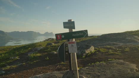 Couple-hiking-past-Husfjellet-trail-sign-on-a-sunny-day-in-Senja-Norway