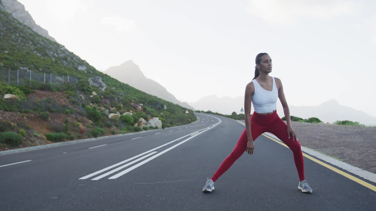 Fit mixed race woman exercising stretching on a country road near mountains
