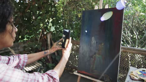 Artista-Birracial-Tomando-Fotos-De-Su-Pintura-Usando-Un-Teléfono-Inteligente-En-Un-Jardín-Soleado,-En-Cámara-Lenta