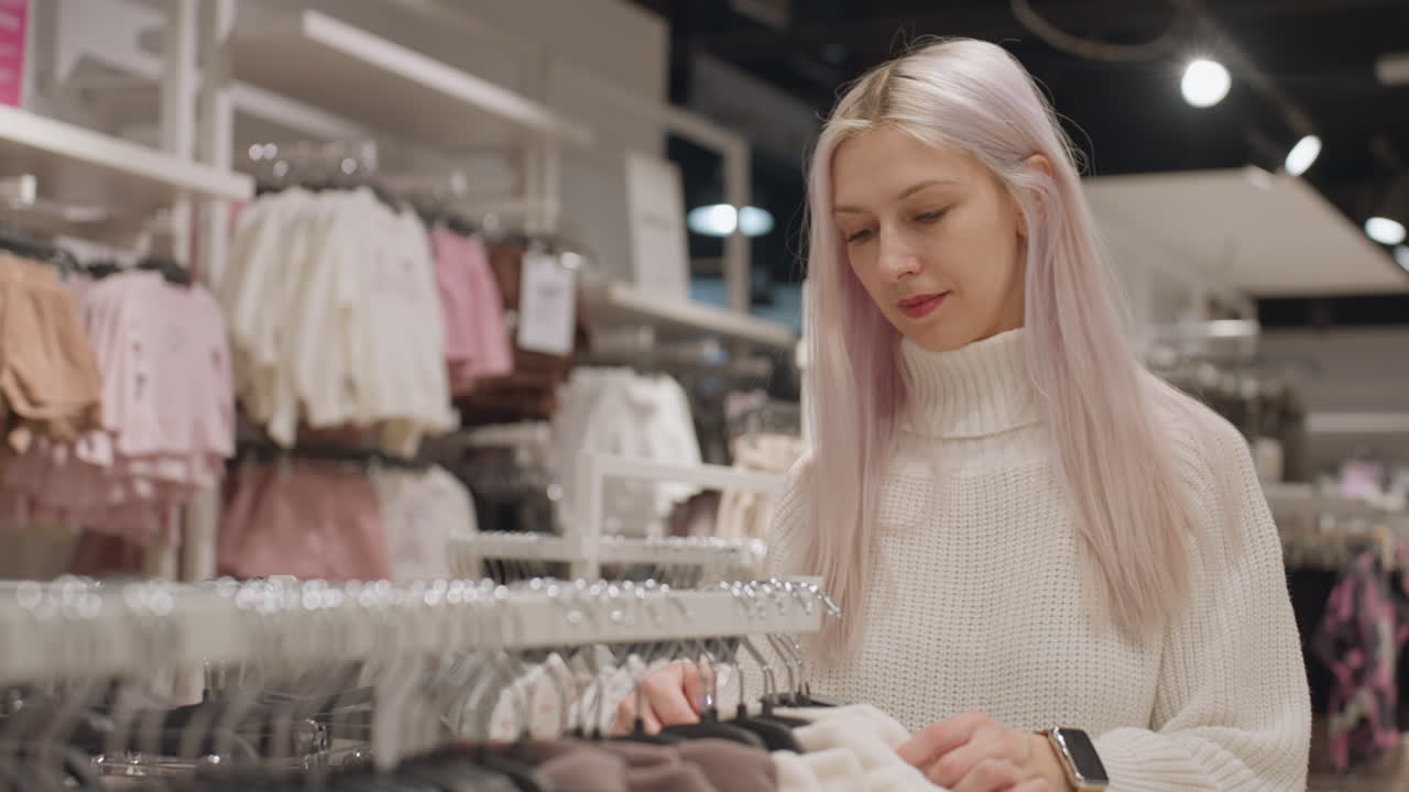 Graceful woman carrying black handbag browses pastel polo rack in upscale boutique gently feels soft fabric selection under warm ambient lighting before making choice with careful focus and elegance
