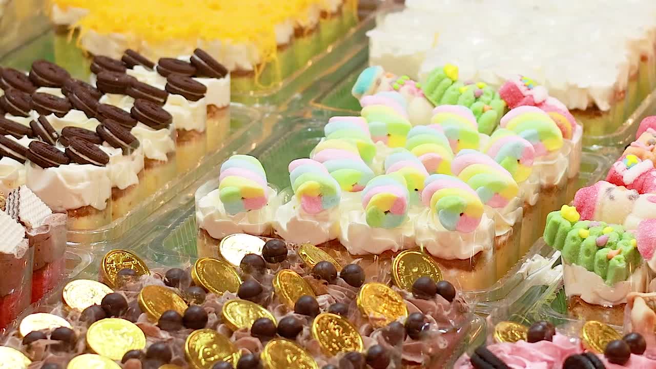 A vibrant display of various miniature cakes, pastries, and sweets arranged in plastic containers