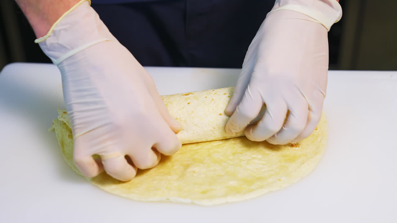 Cooking meat and cheese pita with vegetables. Hands in latex gloves roll up a pita roll. Concept video.