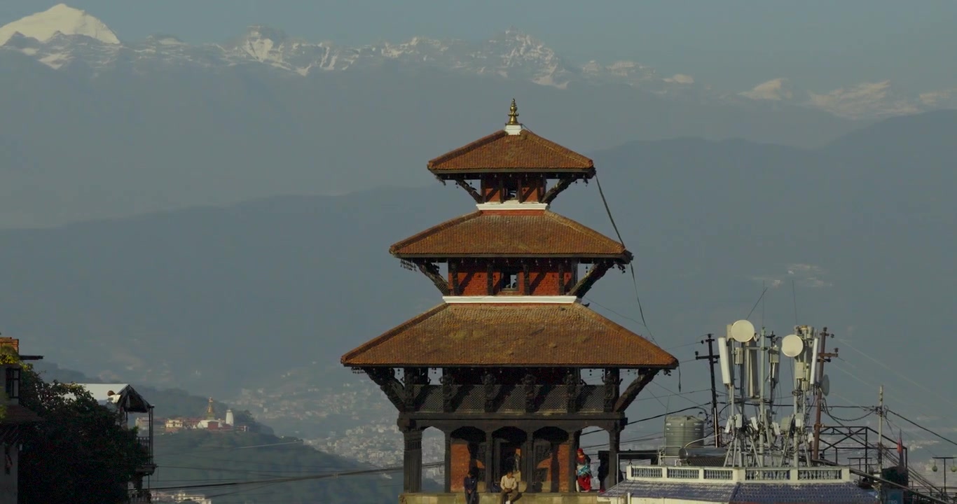 Droneoptagelse fra luften af det historiske Uma Maheshwar hinduistiske tempel i Kirtipur, der viser traditionel pagodearkitektur mod de sneklædte Himalaya-toppe i Kathmandu-dalen, Nepal.