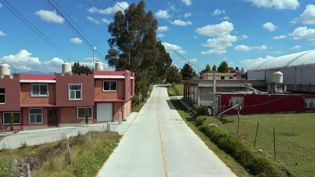 Bird's eye view dolly out over a lonely new road in a rural village on a sunny day, low new houses