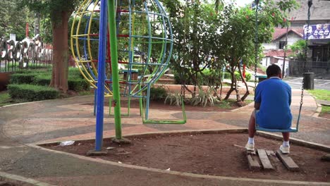 a man sitting on a swing in a city park