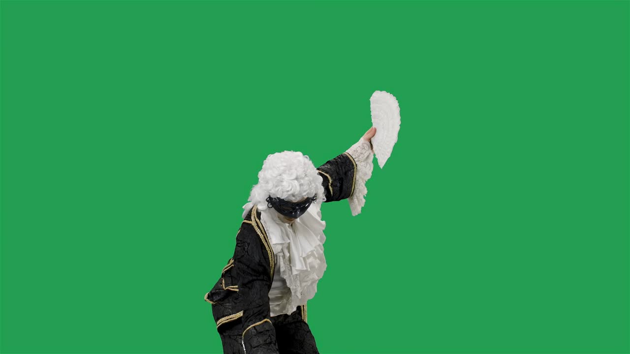 retrato de un caballero cortesano en traje vintage histórico negro, peluca blanca y la máscara inclinándose y haciendo reverencias. joven posando en el estudio con fondo de pantalla verde. cámara lenta