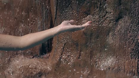 la mano de la mujer atrapa chorros de agua contra la piedra en cámara lenta