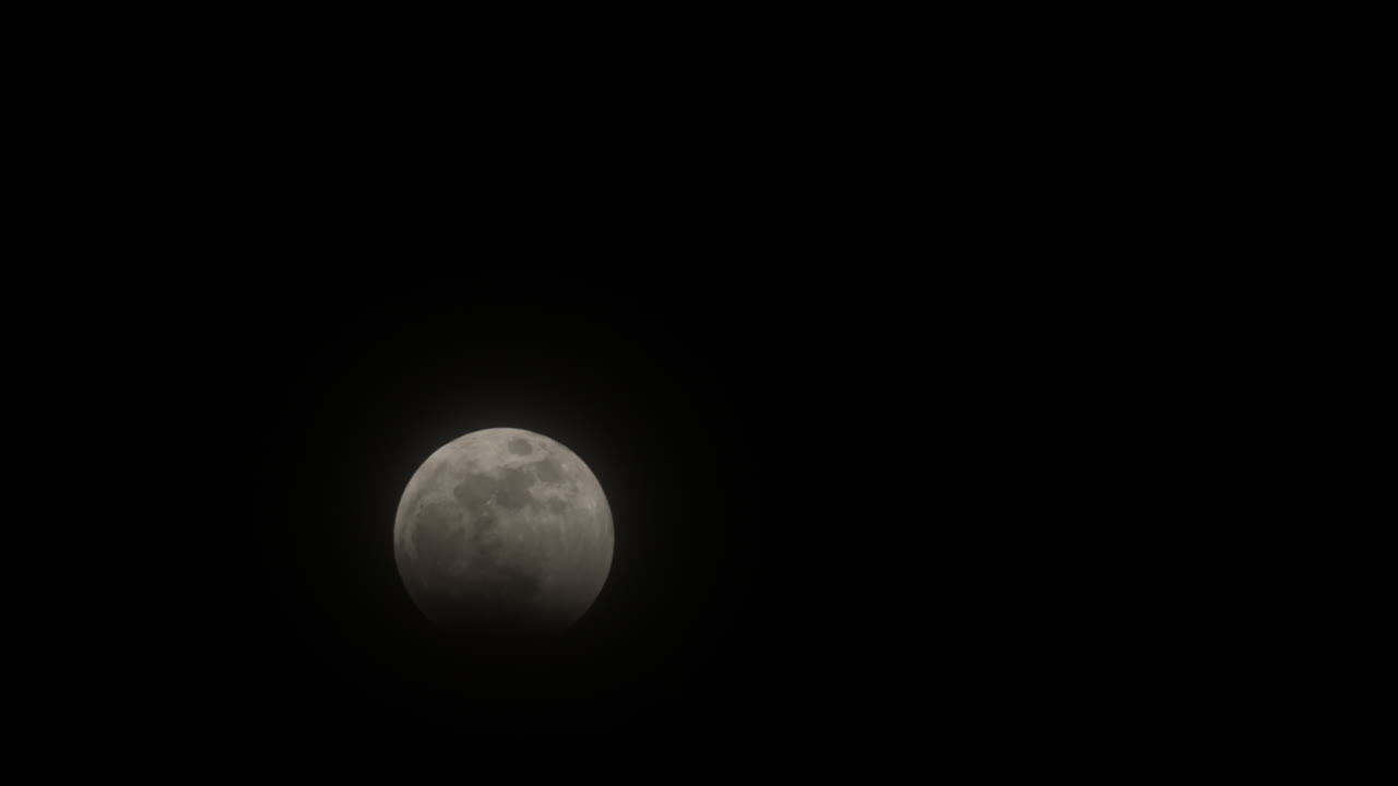 Timelapse of the beginning of the Total Lunar Eclipse on March 14th, 2025 as the moon gets covered in Earth's shadow, with thin clouds passing over it