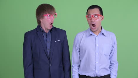 two nerd businessman looking shocked and surprised against green studio background