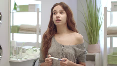 Anxious-young-woman-looks-result-pregnant-test-in-bathroom.-Unplanned-pregnancy