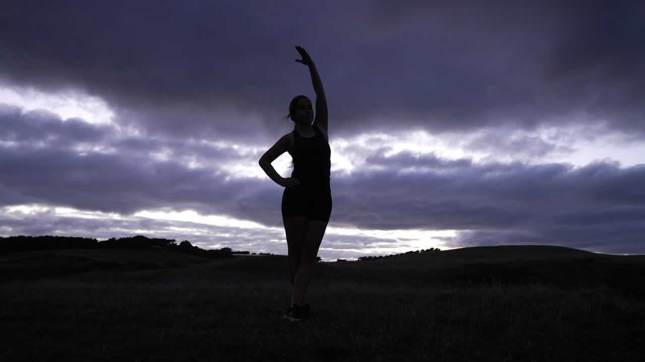 Silhouette of young woman stretching at sunrise