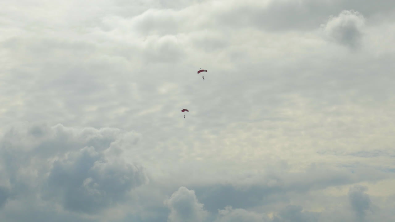 열린 낙하산이 있는 두 명의 단일 스카이다이버가 천천히 땅으로 내려옵니다.